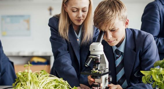 Two upper school pupils looking at plants through a microscope in a UK classroom.