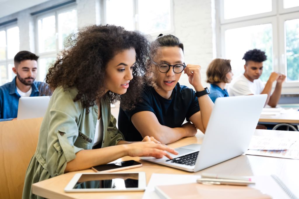 Students in a classroom collaborating in front of a laptop