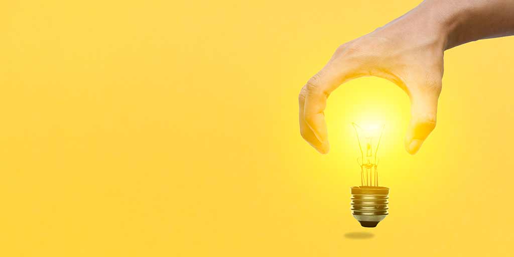 Hand picking up a switched on light bulb