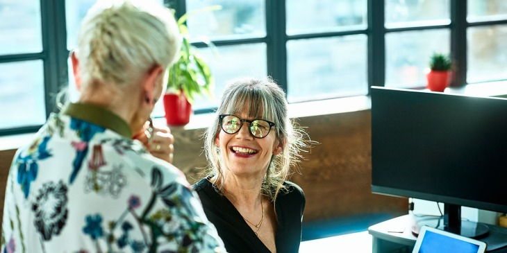 female sat at desk smiling up at a colleague