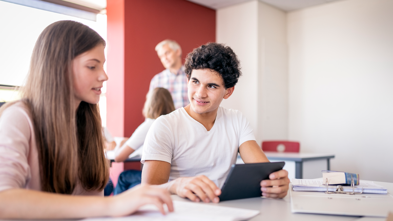 Teenage male and female student in a classroom using a tablet 