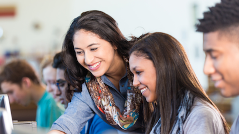 A diverse group of students gathered around a computer screen, engaged and focused on what they see.