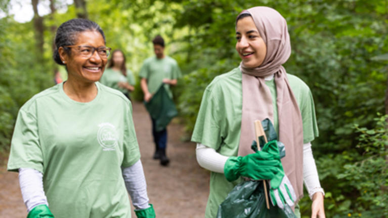 Female volunteers holding bin bags talking with each other while walking through a park and collecting trash.