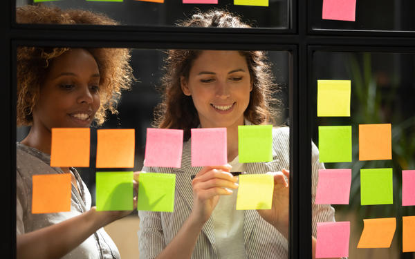 Two team members reviewing a sequence of sticky notes on a window