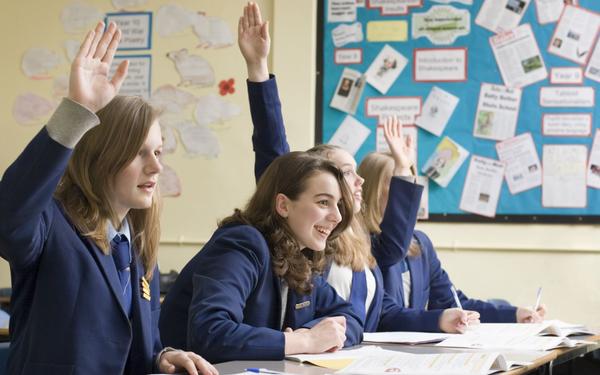 school students smiling at desks wearing blue school uniforms