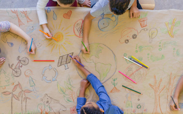 hands of children drawing images of the world and nature with pencils on brown paper