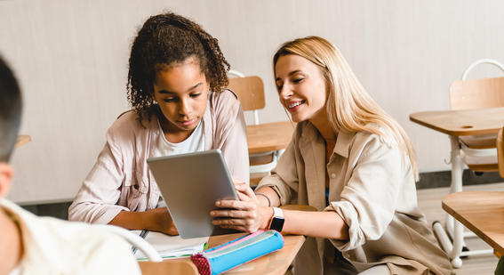 student and smiling teacher looking at an iPad device together in the classroom