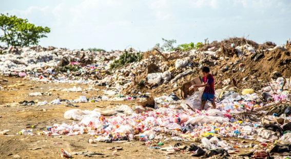Boy holding cardboard box with Plastic waste surrounding him. Photo by Hermes Rivera on Unsplash