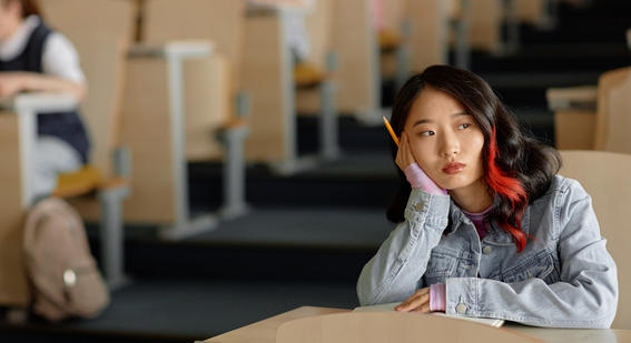 An Asian girl is sitting in an university lecture hall looking worriedly - stock photo