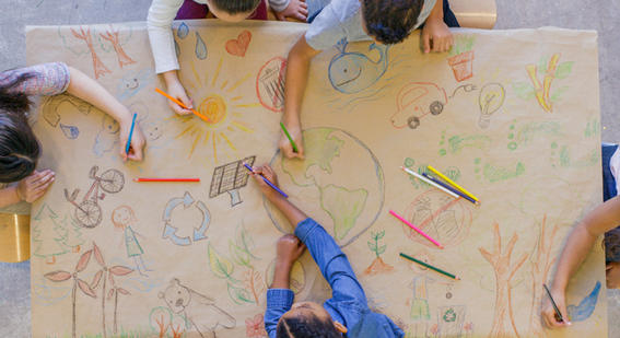 hands of children drawing images of the world and nature with pencils on brown paper
